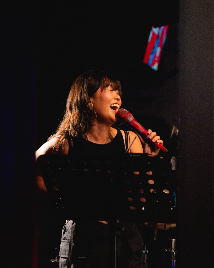 elysrei laughing mid-song on stage, holding a red microphone